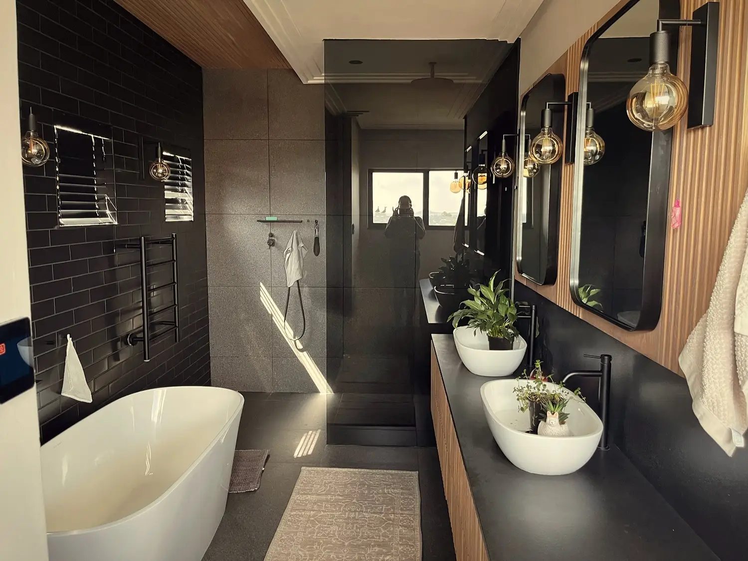 Bathroom with black tiled walls, freestanding tub, brass globe lights